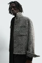Sobrecamisa de corte relajado con textura de tejido estructurado en color gris y negro. Presenta cuello clásico, cierre frontal con botones, mangas largas con puños abotonados y bolsillos de plastrón en el pecho.