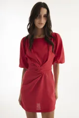 Vestido corto de lino color rojo, con mangas globo y escote redondo. Presenta un corte entallado en la cintura con un lazo ajustable que permite entallar la prenda.