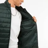 Campera puffer verde oscuro, acolchada, con cuello alto, cierre frontal y bolsillos laterales con cierre.