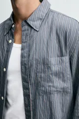 Camisa de corte relajado confeccionada en tejido fluido con mezcla de viscosa, presenta un diseño de rayas verticales, cuello solapa, cierre frontal con botones, manga larga con puño abotonado y un bolsillo de plastrón en el pecho.
