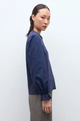 Remera de color blanco con cuello redondo y mangas largas abullonadas que presentan puños con volados.