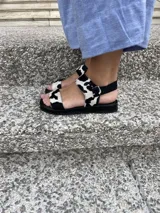 Sandalias bajas con suela negra y tiras de cuero con estampado de vaca.