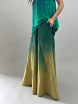 Falda larga de lana con diseño de paneles geométricos y efecto degradado que transiciona de verde esmeralda a tonos amarillentos. Presenta cintura alta, cierre invisible lateral y bolsillos ocultos.