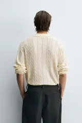 Polo de punto color crema con cuello solapa y abertura frontal, manga larga y diseño de trenzas.