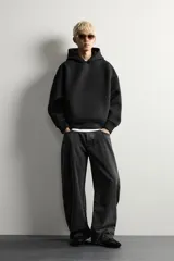 Sudadera negra de corte boxy fit, confeccionada en tejido compacto con elasticidad. Presenta capucha, manga larga, bolsillo frontal tipo canguro y acabados en rib.