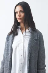Cardigan de tejido de punto gris, con silueta larga, frente abierto, solapas clásicas y bolsillos aplicados en los laterales.