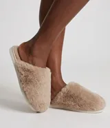Pantufla cerrada de peluche color beige, con suela plana y diseño cómodo para el hogar.
