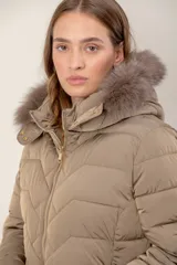 Campera corta capitoneada con diseño de costuras en zigzag, cierre frontal y capucha desmontable con borde de piel sintética. Cuenta con bolsillos laterales con cierre.