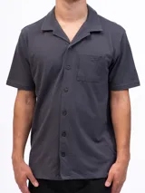 Camisa de manga corta color beige, confeccionada en tejido piqué de algodón, con cuello cubano y un bolsillo de parche en el pecho.