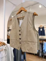 Chaleco sastrero beige con escote en V, botones oscuros en el frente, bolsillos ribeteados y pespuntes en contraste.