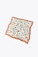 Pañuelo cuadrado de seda o material similar, color base crema, con estampado floral de flores pequeñas en tonos azules, amarillos, naranjas y rosados. Presenta un borde ancho de color terracota o marrón óxido con líneas finas de contraste.