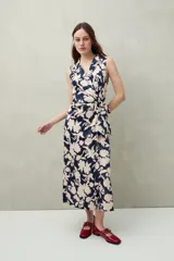 Vestido midi sin mangas con cruce delantero tipo wrap y lazo en la cintura. Presenta cuello sastrero y un estampado floral grande en azul marino y beige claro.