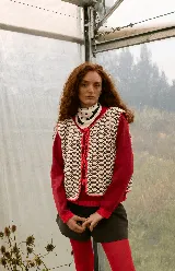 Chaleco tejido a mano en crochet con diseño reversible, presenta un patrón geométrico calado en tonos crema y marrón con terminaciones en color rojo. Cuenta con cierre frontal mediante cordones ajustables.