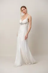 Vestido largo de gasa color marfil, con escote en V, drapeado en el torso y detalle de bordado en pedrería bajo el busto, falda amplia tipo godet y tiritas anchas.