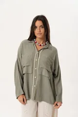 Camisa verde militar de manga larga con silueta oversize, dos bolsillos delanteros y corte levemente más largo en la espalda. Escote en V abotonado con detalle de galón picot a lo largo de la cartera y botones a tono. Isotipo bordado en la parte trasera.