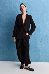 Pantalón negro de tiro alto y calce holgado, con pierna amplia, bolsillos laterales y puños ajustados con botones en los tobillos.
