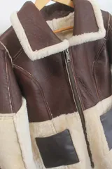 Gamulán reversible de cuero genuino color marrón oscuro con interior de piel sintética en tono crema. Presenta cuello solapa, cierre frontal con cremallera y mangas largas con puños de piel.