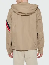 Rompevientos Moncler modelo Claut, color beige, con capucha, cierre frontal y detalle de franjas tricolores en la manga.