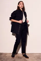 Sobrecamisa negra de algodón con corte oversize, cuello clásico, cierre frontal con botones a presión, dos bolsillos de parche en el pecho y apliques metálicos en cuello y solapa.
