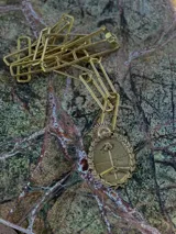 Cadena de eslabones plateados con un dije colgante que representa el Escudo Nacional Argentino enmarcado en una corona de laurel.