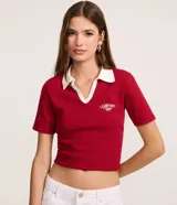 Blusa tipo polo de manga corta, color rojo, con cuello y escote en V con bies blanco contrastante. Presenta una textura gofrada y un bordado pequeño en el pecho con el texto "LE SPORT Paris".
