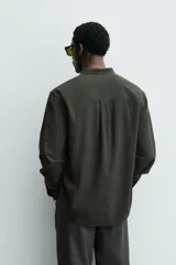 Camisa de corte relajado confeccionada en una mezcla de algodón y modal con acabado efecto arrugado. Presenta cuello tipo tira, cierre frontal con botonadura parcial y manga larga con puños abotonados.
