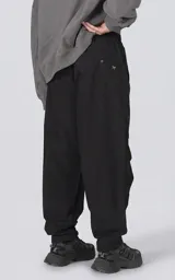 Pantalón de estilo utilitario oversize confeccionado en tejido técnico ripstop. Presenta cintura elástica con broche tipo mochilero, bolsillos cargo frontales de gran tamaño con cierre, bolsillos traseros tipo ojal y sistema de ajuste en los tobillos mediante broches a presión.
