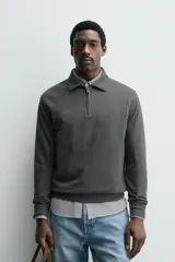 Polo de manga larga color gris oscuro, con diseño de textura estructurada, cuello solapa y cierre frontal de cremallera corta. Cuenta con puños y cintura de rib elástico.