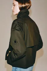 Trench corto Zara Woman Collection confeccionado en hilatura con algodón, en color verde militar. Presenta cuello solapa, manga larga con trabillas y botones en los puños, bolsillos delanteros, bajo asimétrico y cierre frontal cruzado con botones.