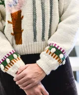 Sweater de punto color blanco crudo, confeccionado en lana merino, con diseño de flores y plantas bordadas y en relieve en tonos rosas y verdes, cuello redondo y mangas largas.