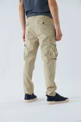 Pantalón cargo color beige, corte slim, con cierre y botón en la cintura, pasacintos, bolsillos cargo con botones y sin puños.