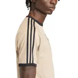 Remera Adidas color beige con cuello redondo y ribetes negros. Presenta las tres rayas características de la marca en negro a lo largo de las mangas raglán y el logo del trébol bordado en el pecho.