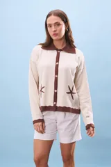 Cárdigan de tejido punto color crema con cuello y ribetes en marrón oscuro. Presenta botones frontales y bordados de estrellas de mar en el frente.