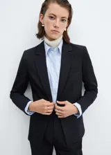 Blazer entallado de color negro con solapas de muesca, hombros estructurados y cierre frontal de un botón. Cuenta con bolsillos de ribete delanteros, detalle de pinzas y abertura posterior.