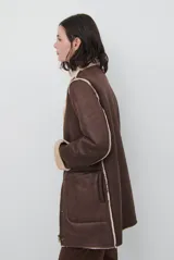 Chaquetón de efecto cuero en color marrón, con interior y detalles en corderito color bordó. Presenta cierre frontal con cremallera y botones a presión, cuello solapa y mangas largas con puños de corderito.