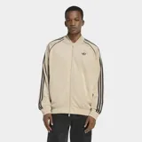 Campera deportiva Adidas Adicolor Classics de corte holgado, color beige con las icónicas tres tiras negras en las mangas y logo del trifolio bordado en el pecho. Cuenta con cierre frontal completo y puños acanalados.