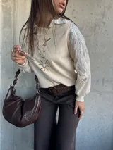 Sweater de punto color natural con cuello polo y mangas largas abullonadas. Presenta detalles bordados con lentejuelas plateadas en los hombros y parte superior de las mangas.