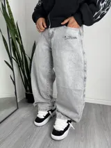 Pantalón de jean estilo baggy, color gris lavado, con corte holgado y amplio. Presenta un pequeño estampado gráfico en la zona del bolsillo delantero.