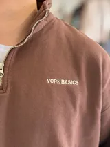 Buzo gris oscuro de corte oversize con cuello alto y cierre frontal parcial. Cuenta con mangas largas y puños elásticos, además de un pequeño bordado con texto en el pecho.