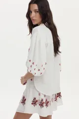 Falda corta blanca de gasa de algodón, con diseño evasé y detalles bordados florales en tonos marrón y naranja.
