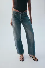 Jeans rectos de tiro medio en denim negro con efecto lavado. Presenta diseño de cinco bolsillos, trabillas para cinto y bajo con vuelta marcada. Cierre frontal con botones metálicos ocultos.