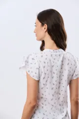 Blusa blanca sin mangas con volados en los hombros, cuello redondo con aberturas y cierre frontal parcial con botones.