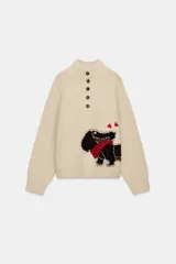 Jersey de punto color beige con cuello subido y cierre frontal de botones. Presenta un bordado de un perro salchicha con una bufanda roja y corazones en la parte inferior delantera.
