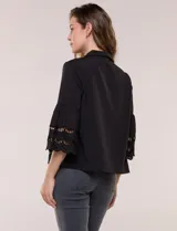 Camisa negra de poliéster con cuello camisero, escote en V y cierre frontal de botones. Cuenta con mangas anchas de corte acampanado y detalles de bordado suizo calado en las mangas y en el ruedo inferior.