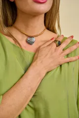 Gargantilla tipo choker con tira de cuero tostado y dije colgante en forma de corazón de metal plateado con grabado floral.