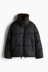 Campera puffer negra oversized con cuello alto forrado en tejido de efecto pelo marrón, bolsillos laterales con botón a presión oculto, cierre frontal y cordón elástico ajustable en el bajo.