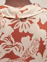 Camisa de manga 3/4 confeccionada en seda viscosa con estampado floral en tonos naranja, rosado y marrón sobre fondo azul marino. Presenta un diseño de corte holgado, cuello camisero y cierre frontal con botones.