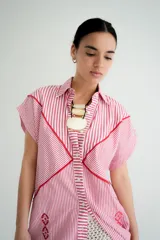 Vestido camisero corto blanco de algodón con bordados negros, cuello camisero, cierre frontal con botones y sin mangas.