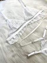 Conjunto de lencería de cuatro piezas en color blanco, confeccionado en encaje con diseño floral. Incluye bralette triangular, tanga de tiro alto con tiras ajustables, portaligas integrado y ligas para las piernas.
