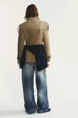 Chaqueta de estilo militar en color beige, con cuello subido, cierre frontal de botones, bolsillos de plastrón con solapa en el delantero y detalle de solapas en el pecho. Presenta mangas largas con hombreras y trabillas decorativas.